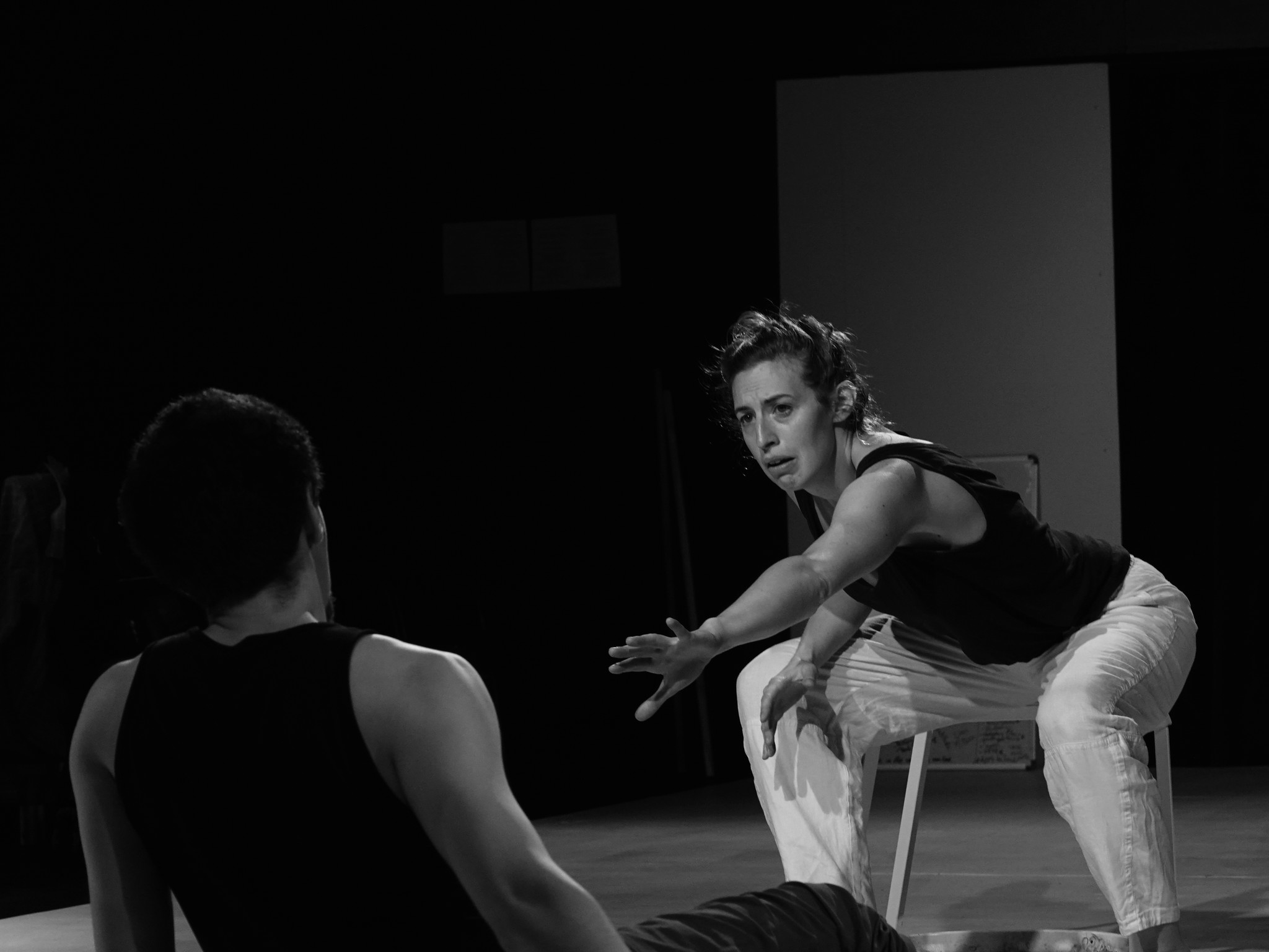 Ariana, in chair, reaches out to Andrew, sitting on the floor & backing away from her, photo by Katrin Talbot